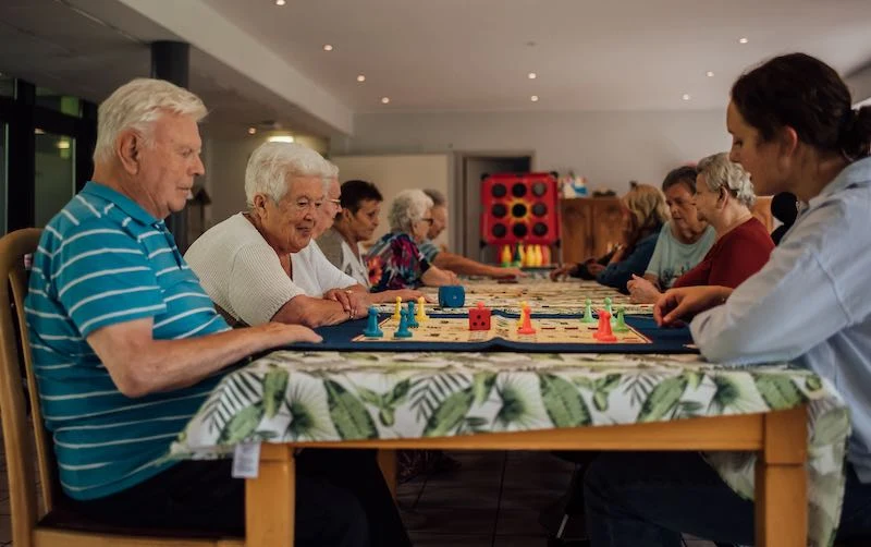 Bewoners spelen samen een bordspel aan tafel in warm licht