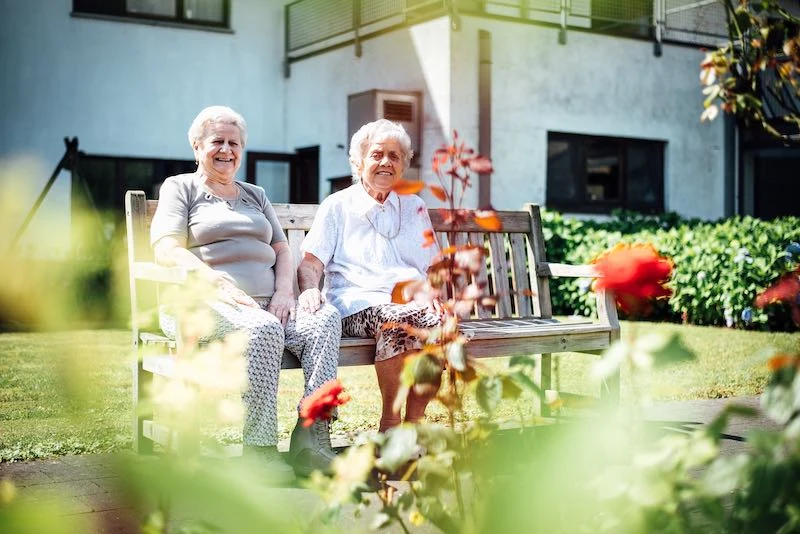 Twee ouderen op een bankje in de tuin voor een wit gebouw