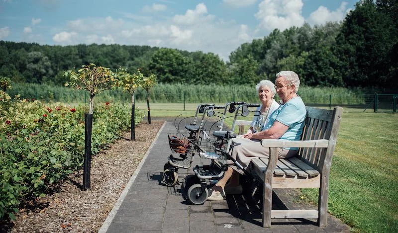 Twee bewoners op een houten bank met uitzicht op fruitbomen en weilanden