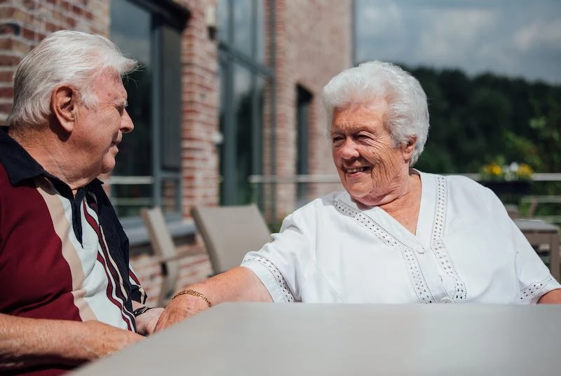 Twee bewoners in gesprek aan een tafel op het terras achter het gebouw