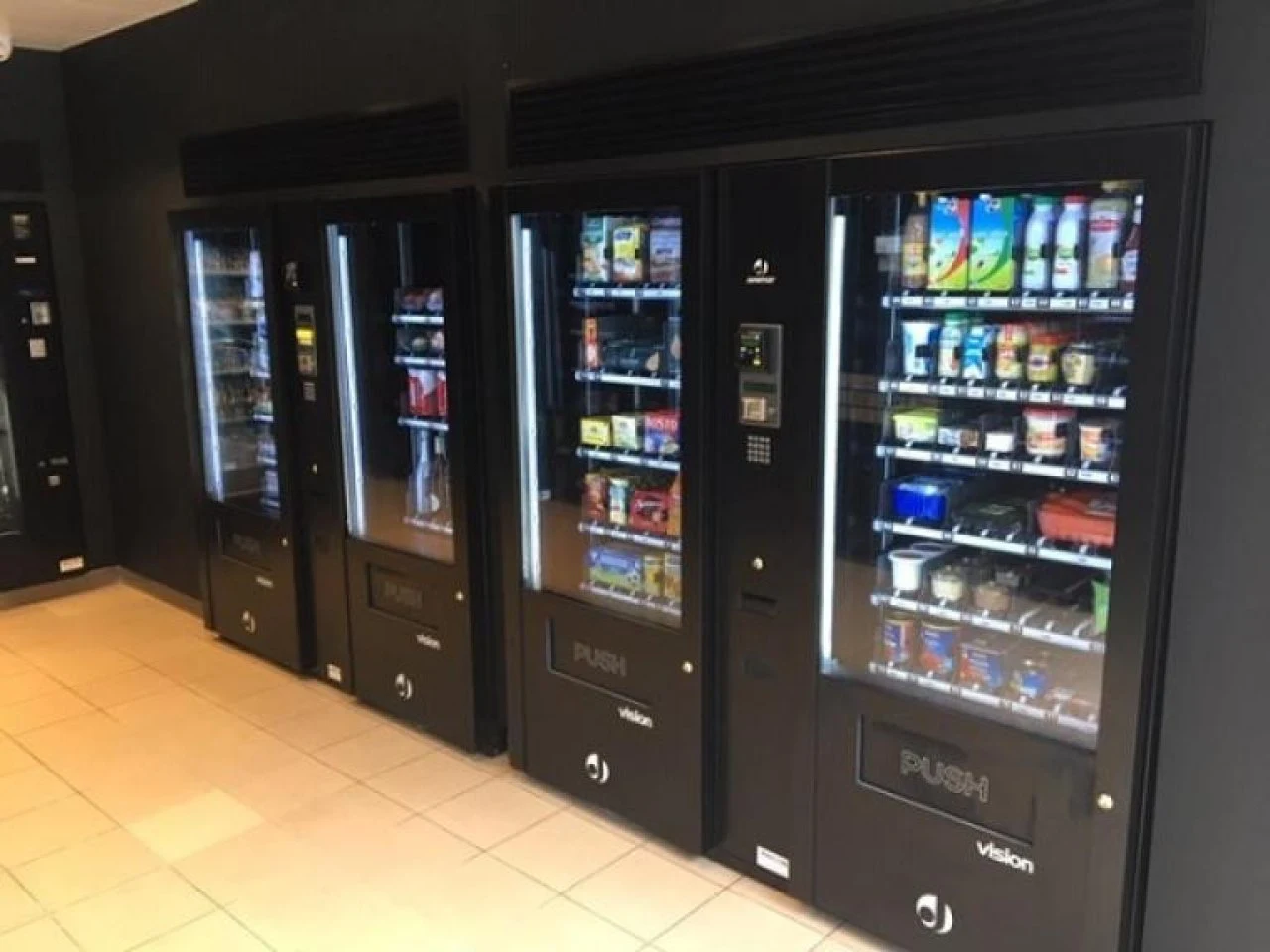 Rij van vier automaten met glazen front in een bedrijfsgang