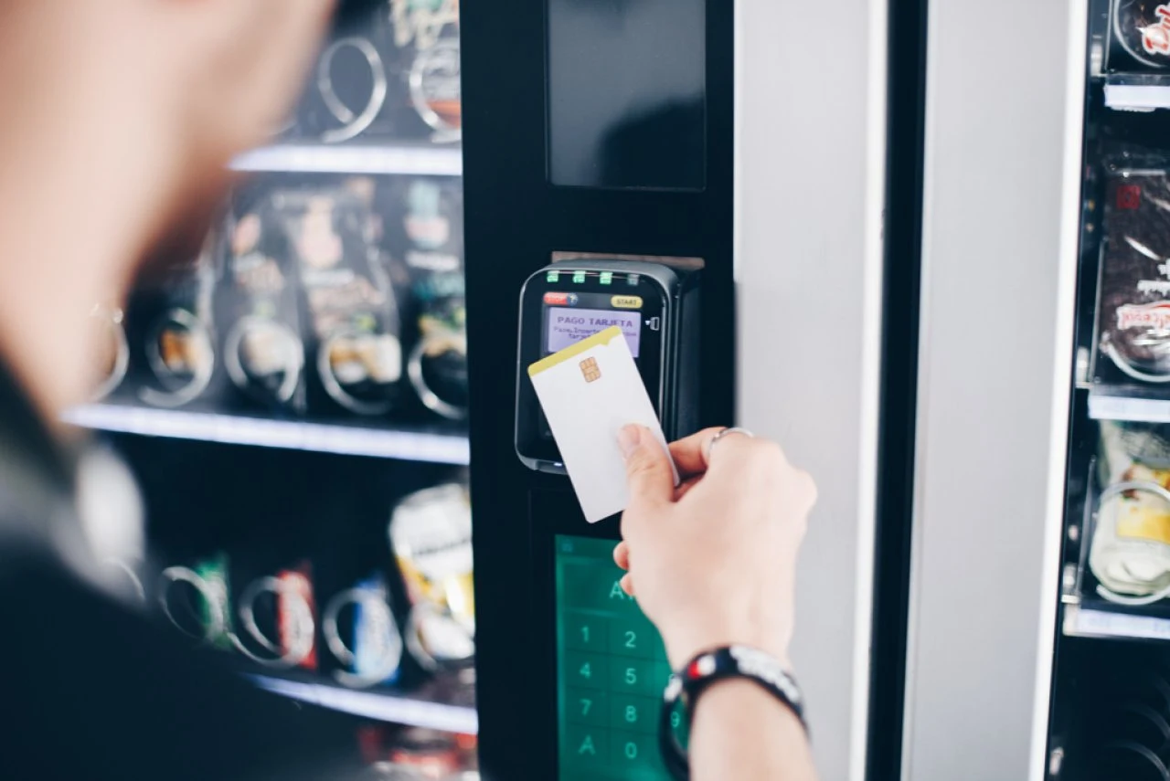 Hand houdt een bankkaart voor de contactloze lezer van een gekoelde drankautomaat