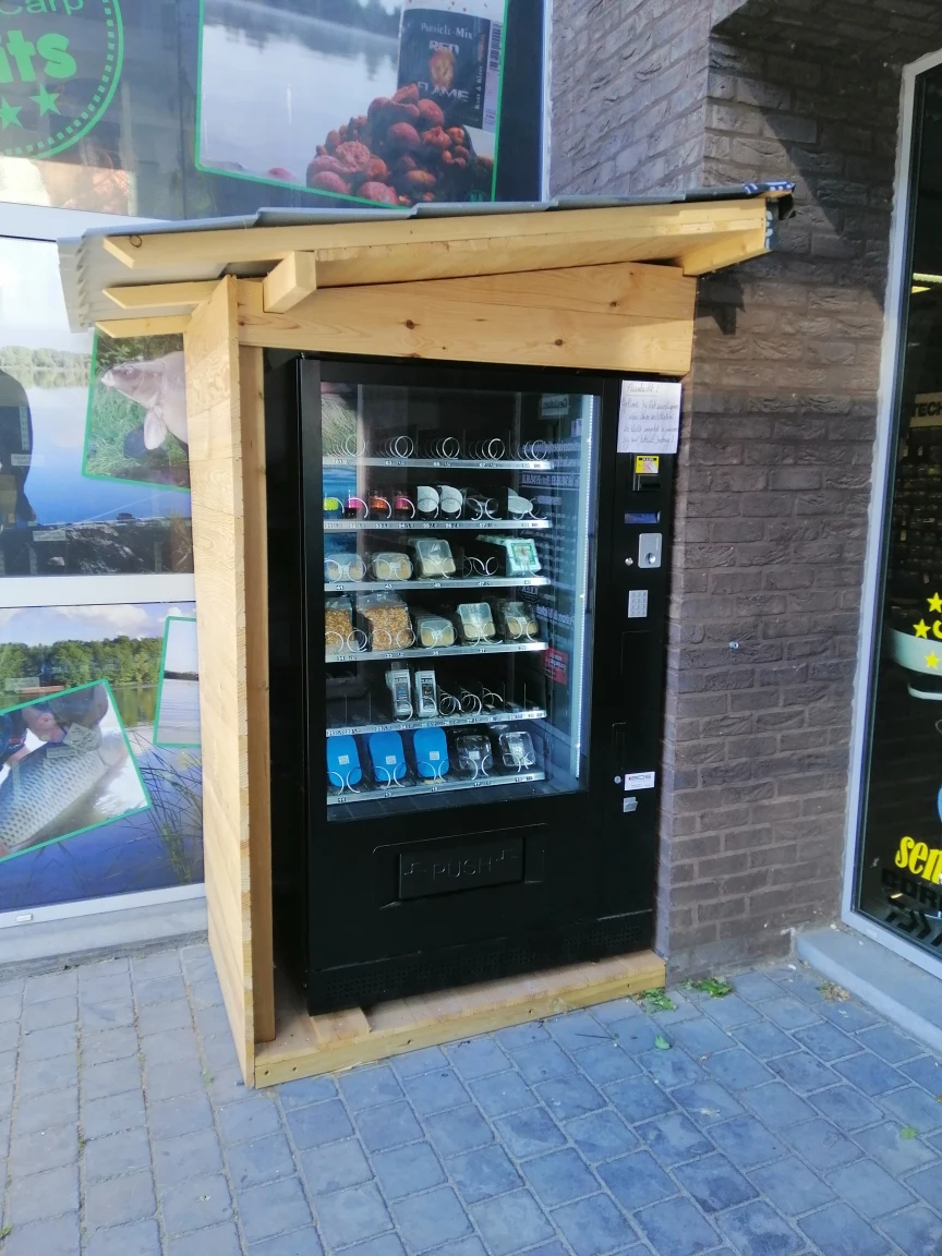 Automaat met houten overkapping tegen een bakstenen muur, gevuld met visgerei