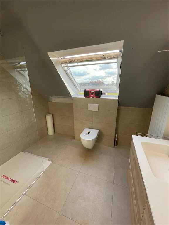 Badkamer onder het dak met beige tegels